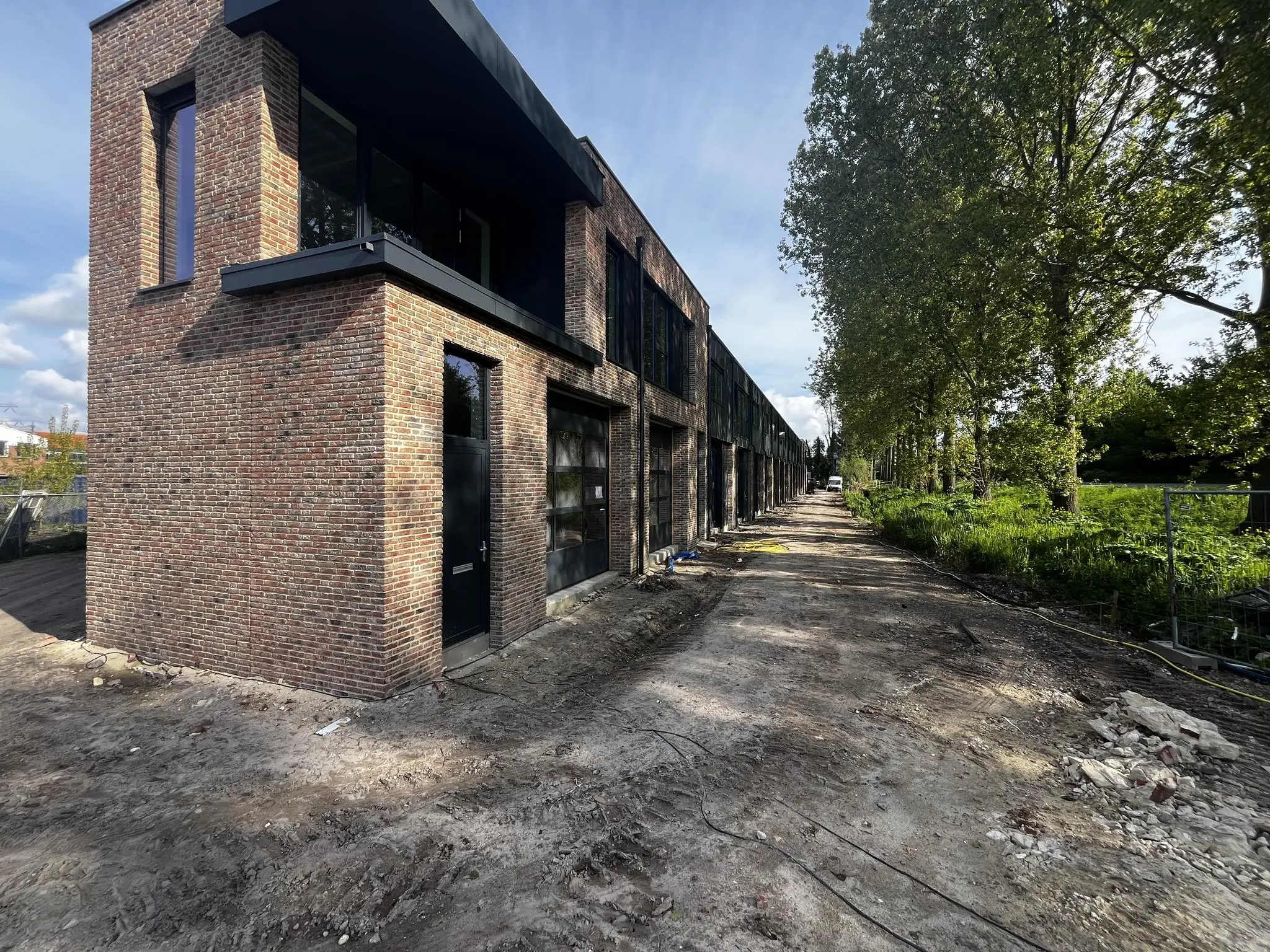Nieuwbouw huizen aan de Broekdijk-West in aanbouw met een onverharde weg en bomenrij ernaast.